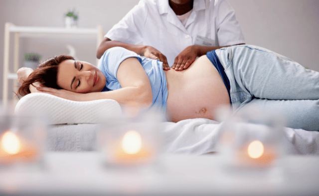 A pregnant woman lying on her side, supported by cushions, receiving a gentle prenatal massage in a calm and well-lit spa environment.